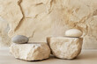 © Victoria - Two smooth stones sit atop beige rock pedestals set against a textured wall, creating a serene and minimalist backdrop