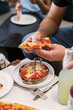 © Kat Schleicher/Stocksy - Hand Holding a Slice of Pepperoni Pizza at a Restaurant Table