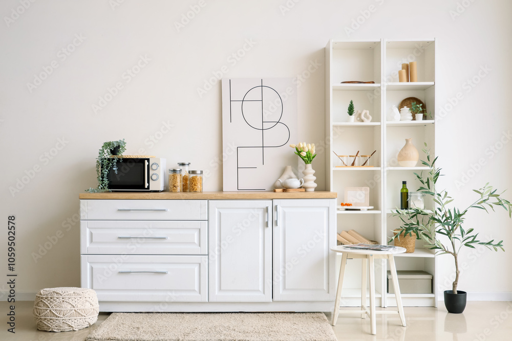 White counters, microwave oven, shelving unit and picture in interior of kitchen