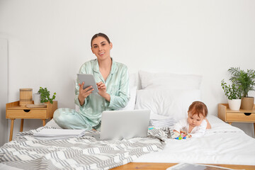 Poster - Young happy business mother in pajamas working with gadgets and little baby playing at home