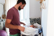 © Raul Navarro/Stocksy - Father changing his newborn baby on changing table at home