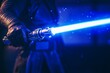 © InfiniteStudio - A man grips a bright blue lightsaber, showcasing power and creativity in a dynamic action pose in a dimly lit environment