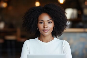 Poster - A confident woman with curly hair smiles while seated at her desk in a modern office environment, suggesting professionalism and approachability.
