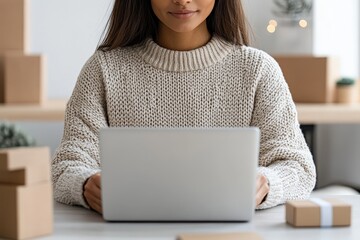 Poster - A woman in a cream sweater uses a laptop in a cozy home office setting with cardboard boxes, possibly handling online shopping or business tasks.