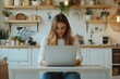 © Odin AI - A focused woman sits at a table in a stylish kitchen, working on her laptop. Surroundings include modern shelves, plants, and stylish decor, exuding calmness.