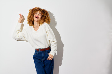 Happy woman laughing in a white sweater and blue jeans against a light background, showcasing a joyful and carefree spirit, perfect for lifestyle and fashion themes