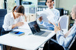 © NanSan - A Muslim businesswoman sits with an Asian man and woman, all middle-aged, at a desk with a laptop, appearing stressed as they discuss challenging business matters in a corporate setting