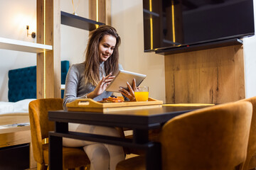 Woman in her home eating dessert. She is using her tablet while taking a break from the food.