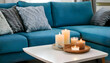 © Khaisan - Close up of candles on white coffee table near blue sofa. Scandinavian home interior design