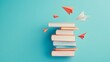 © milkyway - Stacked Books and Paper Airplanes Against Vibrant Teal Background