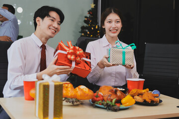 full length view of a group of business team wearing red Santa hat and exchange gift box together in the office for Christmas.