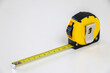 © Adam - Black and yellow retractable tape measure held in place at 10 cm, on white background, useful tool for measuring length, width and height. Accuracy and precision concept