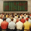 © PuiZera - A crowd of people watch a stock ticker in a trading room.