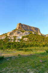 Wall Mural - a rugged cliff rises above a green landscape under a clear blue sky