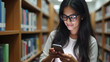 © fotoluigi868 - Young Indian student types on her smartphone in a university library.