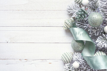 Poster - Christmas side border of soft green ornaments, ribbon, and snowy tree branches. Top down view on a white wood background. Copy space.