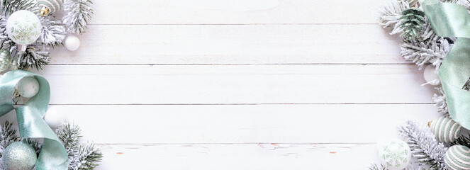 Poster - Christmas double border of soft green ornaments, ribbon, and snowy tree branches. Top view on a white wood banner background. Copy space.