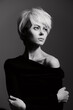 © SHOTPRIME STUDIO - Elegant young woman with short blonde hair, wearing a black off-shoulder top, posing thoughtfully against a dark background. Artistic portrait conveying introspection.