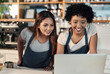 © peopleimages.com - Women, waitress and happy with laptop at cafe on counter for online orders, ecommerce and purchase. People, employees and smile at coffee shop as barista on internet for social media reviews on menu