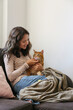 © Evrymmnt - Brunette young woman playing with her rescue red cat at home. Copy space background.