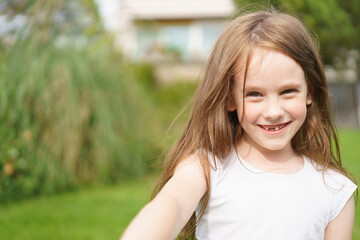 Little cheerful girl without one front tooth wearing a t-shirt in the backyard of her house in summer. Concept of children's fun, health, education, safety and insurance