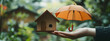 © imran - Hand holding an umbrella over a wooden house model, symbolizing protection in real estate and insurance  -