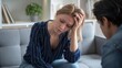 © Needless - A woman holding her head in her hand, appearing stressed during therapy with male psychologist