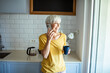 © Marko Geber - Senior woman using smartphone while drinking morning coffee in kitchen