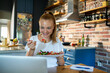 © Geber86 - Woman using laptop on kitchen table while eating healthy meal