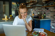 © Geber86 - Woman using laptop on kitchen table while eating healthy meal