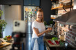 © Geber86 - Young woman filming cooking tutorial in kitchen with fresh vegetables and eggs