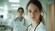 © sirisakboakaew - Friendly female healthcare worker in a hospital, looking at the camera with a professional demeanor, with a supportive colleague in the background