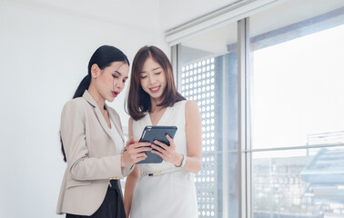 Wall Mural - Business portrait two person woman asian standing smile cheerful talk looking holding tablet and hands up happy with in agreement ready new project marketing job for work in room office company