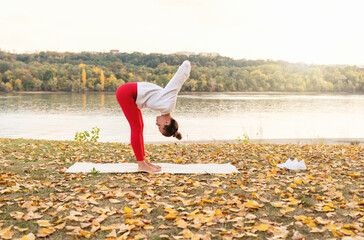 Wall Mural - Outdoors workout. Woman practicing yoga stretching exercise by the riverside in nature. Healthy lifestyle.