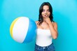 © luismolinero - Young hispanic woman holding beach ball isolated on blue background happy and smiling covering mouth with hand
