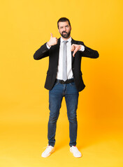 Wall Mural - Full-length shot of business man over isolated yellow background making good-bad sign. Undecided between yes or not