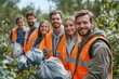 © SerPak - A cheerful group of volunteers gathers in a lush forest, dressed in matching orange vests and holding trash bags. Their smiles reflect a shared commitment to cleaning up the environment under the warm