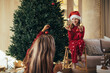© polinaloves - Beautiful young mother and her 7-years old daughter decorating Christmas tree in a festive living room.