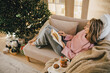 © polinaloves - Young woman relaxing, reading book and drinking cocoa in a cozy living room near Christmas tree.