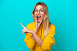 © luismolinero - Young Uruguayan woman isolated on blue background pointing to the side to present a product and whispering something