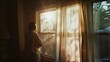 © VK Studio - A solitary figure gazes out a window, the warm golden glow of sunlight filtering through gauzy curtains, creating a serene and introspective mood.