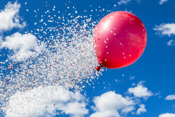 Red Balloon Bursting with Confetti in Blue Sky.