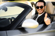 © Minerva Studio - Confident young man in stylish sunglasses and suit gives a thumbs up from the driver's seat of a luxury convertible car, exuding positivity and success