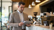 © Abubakar - A business professional standing at a modern caf?(C) counter, holding a digital tablet and reviewing documents