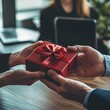 © Юлія Корніенко - A professional setting where a red gift box is exchanged between two individuals, symbolizing appreciation and teamwork in a business environment.