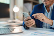 © amnaj - Businessman using smartphone and reading charts while working at desk in modern office