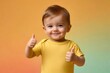 © NusratJahan - Smiling toddler in yellow t-shirt showing thumbs-up on colorful background
