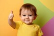 © NusratJahan - Smiling toddler in yellow t-shirt showing thumbs-up on colorful background