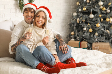 Canvas Print - Happy young couple hugging on bed with champagne glasses in bedroom decorated for Christmas celebration