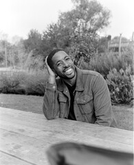 Happy man smiling and leaning on wooden table in black and white